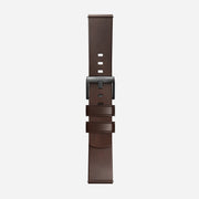 The Nomad Active Band Pro is a 22mm quick release brown Horween leather strap with black hardware, featuring adjustment holes and two loops to secure excess length, displayed vertically on a plain white background.