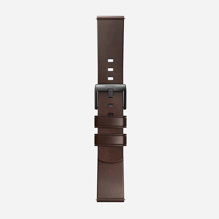The Nomad Active Band Pro is a 22mm quick release brown Horween leather strap with black hardware, featuring adjustment holes and two loops to secure excess length, displayed vertically on a plain white background.