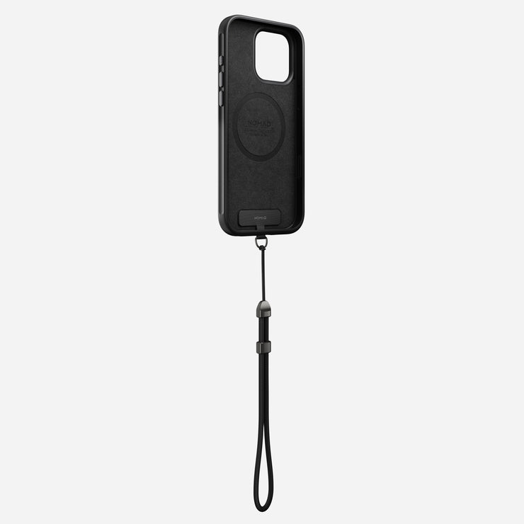 The Nomad Wrist Strap - Kevlar | Carbide is a black smartphone case with electroplated metal hardware, a wrist strap, and a camera cutout. Displayed upright on a light gray background, it features a circular design at the center.