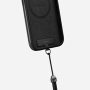 A close-up of the Nomad Wrist Strap - Kevlar | Carbide, featuring a detachable black lanyard and electroplated metal hardware, attached to a black phone case against a plain light background.
