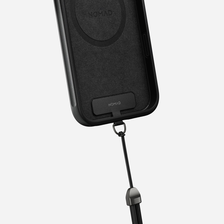 A close-up of the Nomad Wrist Strap - Kevlar | Carbide, featuring a detachable black lanyard and electroplated metal hardware, attached to a black phone case against a plain light background.