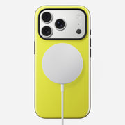A yellow iPhone 17 Pro in the Volt color is shown from the back, protected by Nomad's Modern Case. A MagSafe circular wireless charger is magnetically attached at the center, its cable extending downward. Three rear cameras are visible.