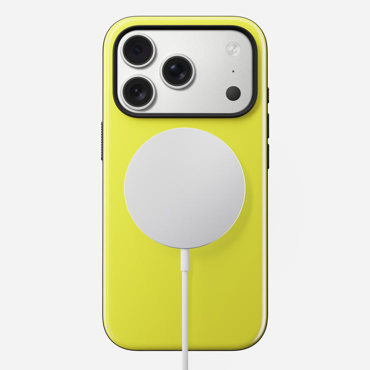 A yellow iPhone 17 Pro in the Volt color is shown from the back, protected by Nomad's Modern Case. A MagSafe circular wireless charger is magnetically attached at the center, its cable extending downward. Three rear cameras are visible.
