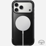 The Nomad Rugged Leather Case for iPhone 17 Pro Max in black Horween leather features a MagSafe-compatible design for easy wireless charging, with the logo at the bottom right and shown here with a silver phone and white MagSafe charger.