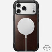 The Nomad Rugged Leather Case for iPhone 17 Pro Max in Rustic Brown features a Horween leather panel with black edges, MagSafe-compatible round charger attached, and displays the Horween logo at the bottom right.