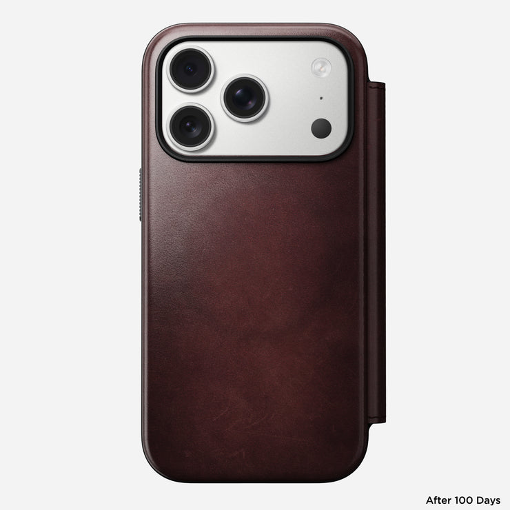 The Nomad Modern Leather Folio for iPhone 17 Pro, shown in burgundy Horween leather with a visible fold and exposed camera lenses, is photographed from the back on a plain white background with "After 100 Days" in small text at bottom right.