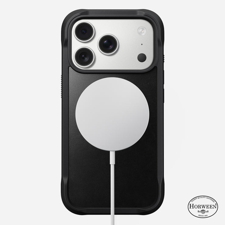 A Nomad Rugged Leather Case for iPhone 17 Pro in black, made from Horween leather, is shown face down with three camera lenses and a circular MagSafe-compatible charger attached to the back.