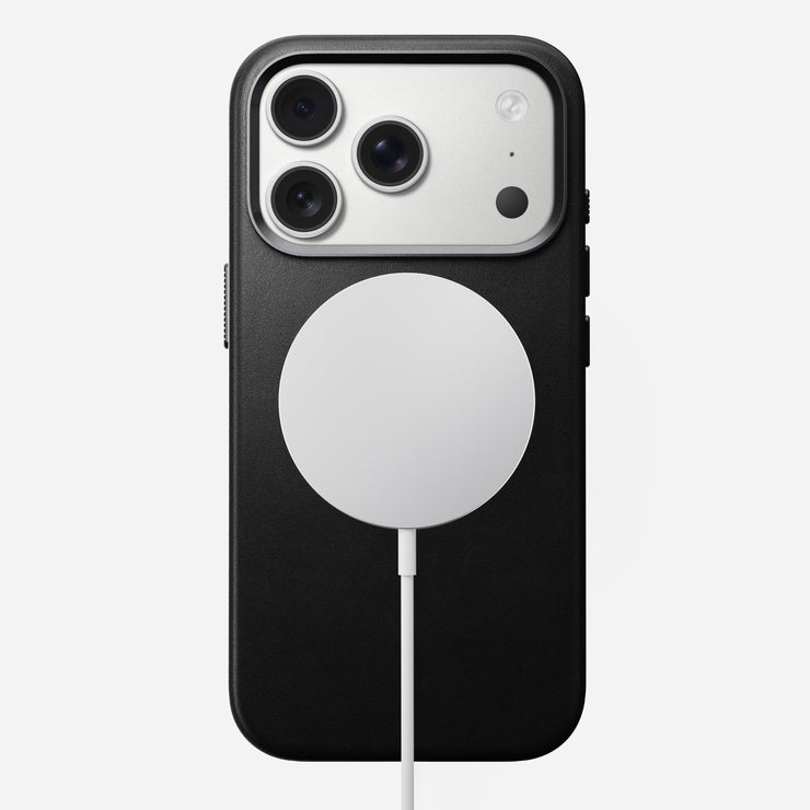 A Nomad Traditional Leather Case in black is shown on an iPhone 17 Pro, featuring three rear cameras and a circular white MagSafe charger attached to the back, all against a plain white background.