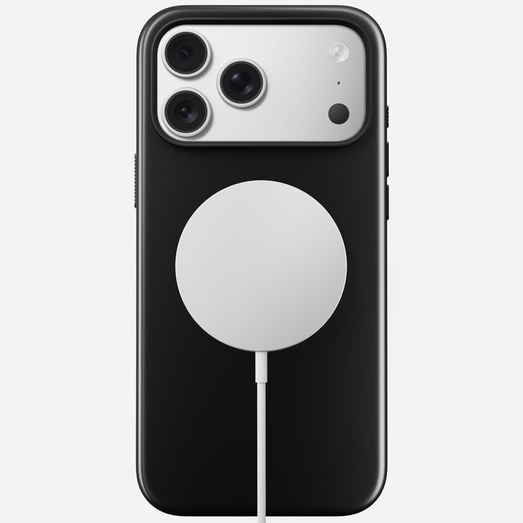 A Nomad Modern Case - iPhone 17 Pro Max in Vulcan Black with TPU bumper (8ft drop protection), triple cameras, and a silver MagSafe charger connected by a white cable, shown on a plain white background.