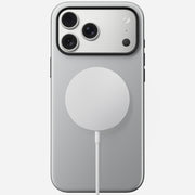The Nomad Modern Case for iPhone 17 Pro Max in Lunar Gray adds drop protection with a sleek TPU bumper, wrapping the silver phone’s back while it charges on a round, white MagSafe-compatible wireless charger.