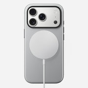 The Nomad Modern Case - iPhone 17 Pro in Lunar Gray is shown from the back with a round, white wireless charger attached. The MagSafe compatible phone has three rear cameras in the top left, set against a plain white background.