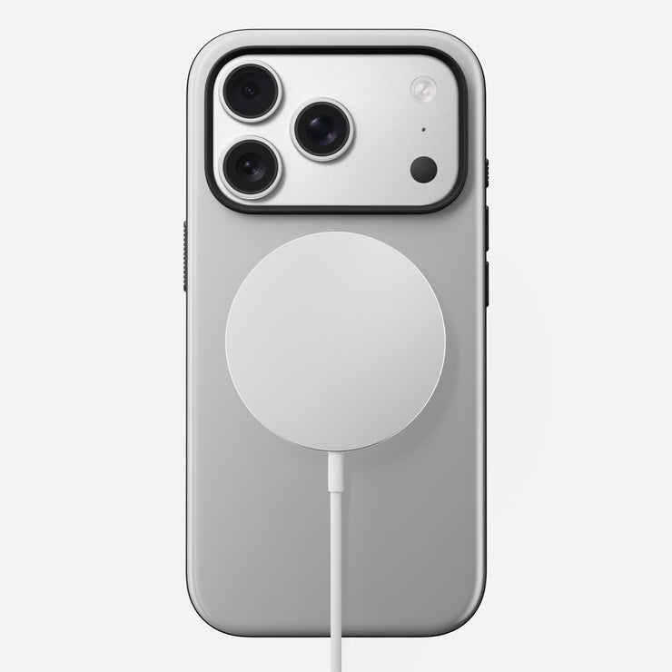 The Nomad Modern Case - iPhone 17 Pro in Lunar Gray is shown from the back with a round, white wireless charger attached. The MagSafe compatible phone has three rear cameras in the top left, set against a plain white background.