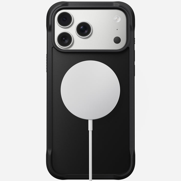 A Nomad Rugged Case for iPhone 17 Pro Max in black, with TPU bumpers, is shown from the back against a plain background. A round white MagSafe wireless charger is attached below the camera module.