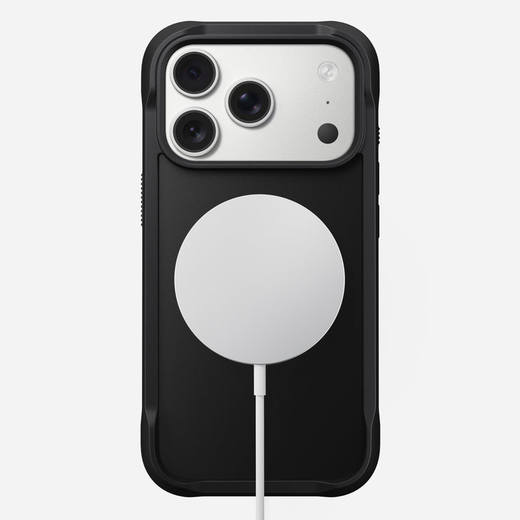 The Nomad Rugged Case for iPhone 17 Pro in black is shown from the back, displaying three rear camera lenses in the top left corner and a round white MagSafe-compatible wireless charging pad attached at the center.