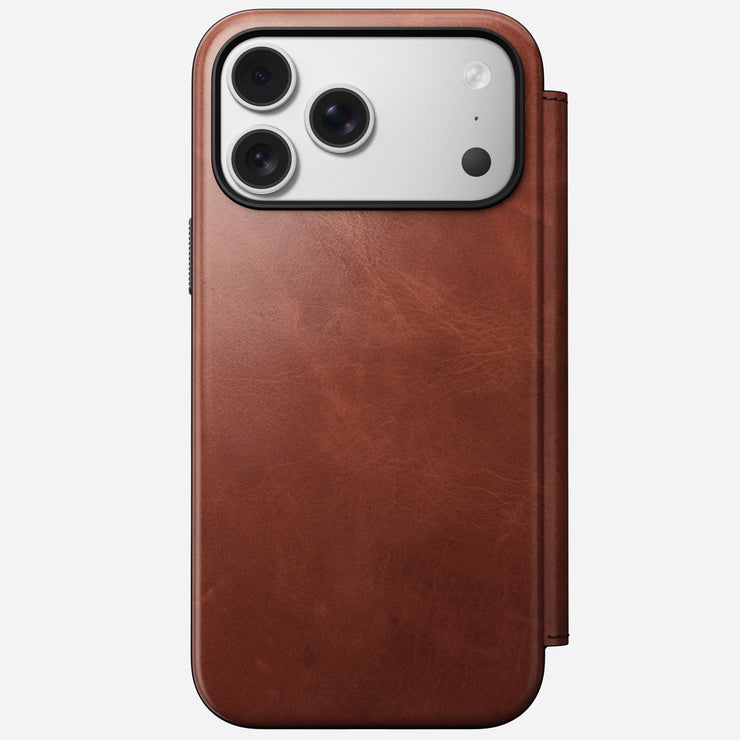 A Nomad Modern Leather Folio in Olde Dublin Horween leather covers an iPhone 17 Pro Max, showing the triple-lens camera and flash. The brown MagSafe-compatible case features a magnetic cover for easy charging.
