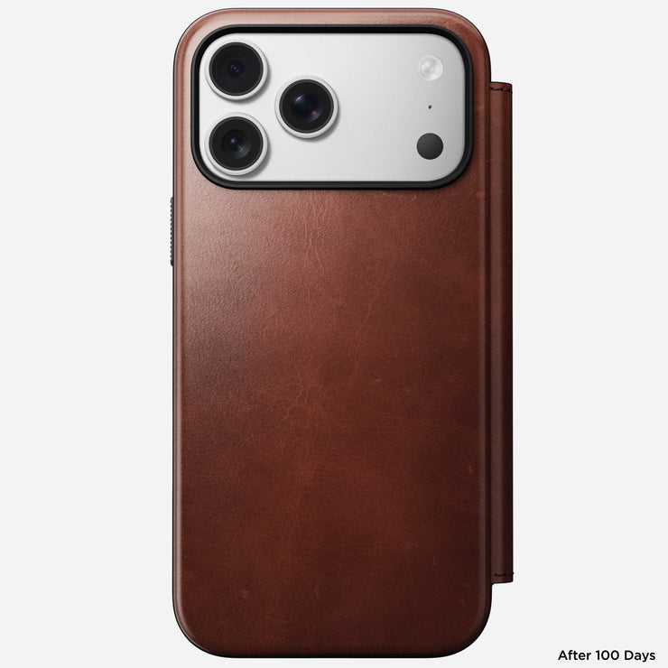 The Nomad Modern Leather Folio for iPhone 17 Pro Max in Olde Dublin Horween leather covers a triple-lens phone, showing a smooth patina and "After 100 Days" at the bottom right. MagSafe compatible for seamless wireless charging.