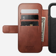 A brown Nomad Modern Leather Folio for iPhone 17 Pro in Olde Dublin Horween leather, featuring three card slots with two cards and a partially visible U.S. dollar bill; the phone slot is empty.