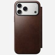 The Nomad Modern Leather Folio for iPhone 17 Pro Max in Rustic Brown Horween leather displays the phone's triple camera lenses from the back, set against a plain white background.