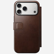 The Nomad Modern Leather Folio for iPhone 17 Pro Max in Rustic Brown (Horween) showcases a triple-lens camera partially visible in a MagSafe compatible wallet case with stitched magnetic clasp, set against a light background.