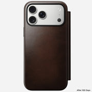 An iPhone 17 Pro Max in a Nomad Modern Leather Folio (Rustic Brown, Horween) displays its three rear cameras and worn, smooth leather finish. "After 100 Days" appears in the bottom right corner.