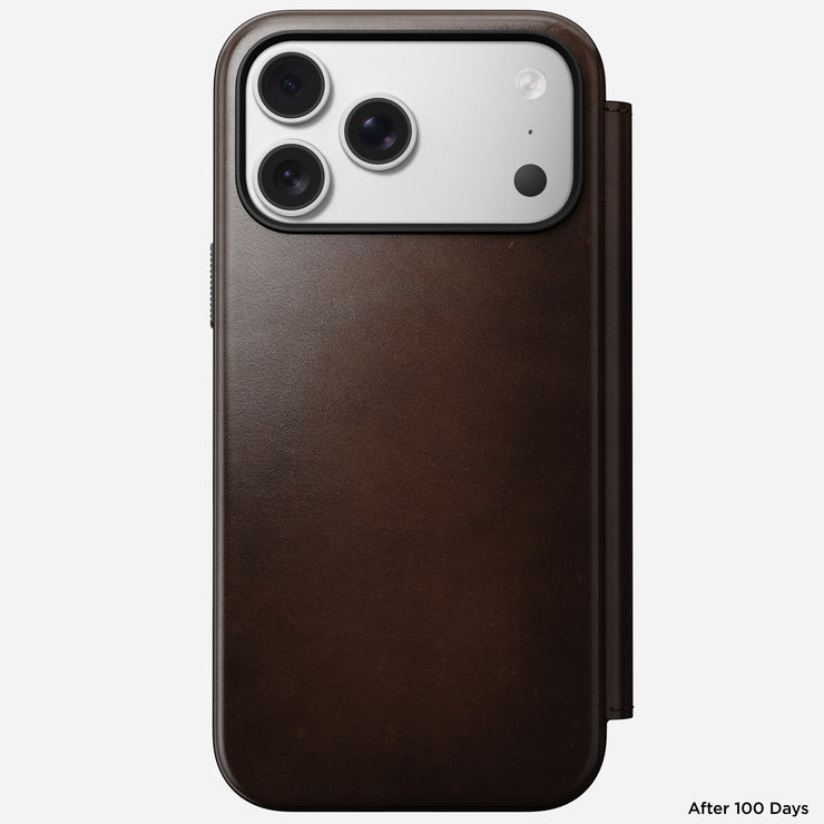 An iPhone 17 Pro Max in a Nomad Modern Leather Folio (Rustic Brown, Horween) displays its three rear cameras and worn, smooth leather finish. "After 100 Days" appears in the bottom right corner.