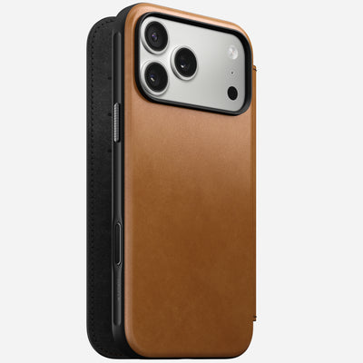 The Nomad Modern Leather Folio for iPhone 17 Pro Max in English Tan-C is shown standing upright, with its full-grain leather cover slightly open to reveal side buttons and the phone's three rear cameras.