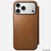 The Nomad Modern Leather Folio in English Tan-C covers an iPhone 17 Pro Max with three rear cameras and a flash. The full-grain leather case shows slight wear. "After 100 Days" is inscribed in the bottom right corner.