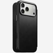A Nomad Modern Leather Folio in black, designed for iPhone 17 Pro Max, stands upright with its case slightly open, revealing the phone’s triple-lens rear camera and flash against a plain white background.