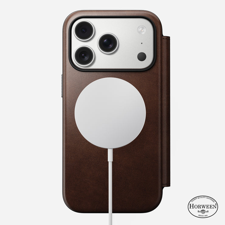 A Nomad Modern Leather Folio in Rustic Brown Horween leather is on an iPhone 17 Pro with three rear cameras, attached to a round MagSafe-compatible wireless charger. The Horween Leather Company logo appears at the bottom right.