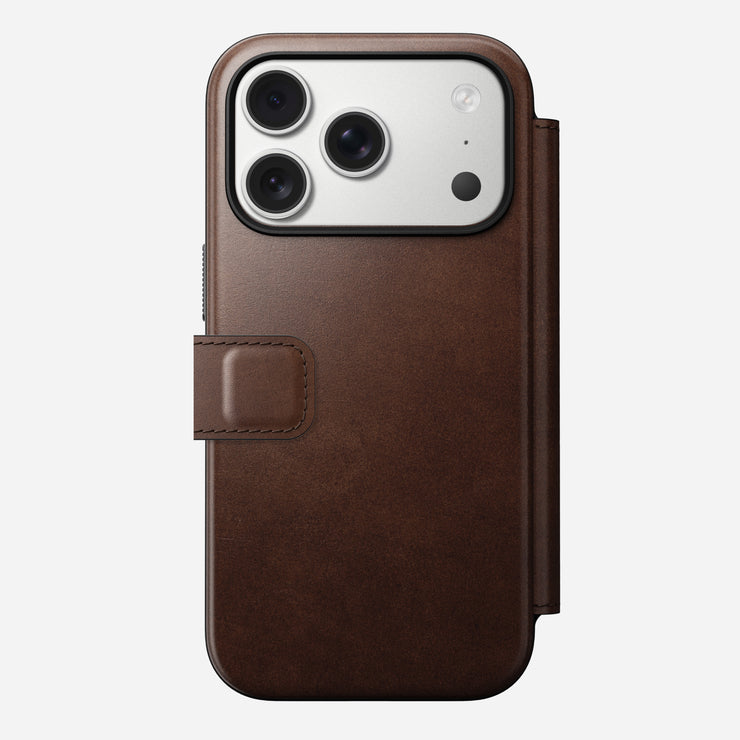 The Nomad Modern Leather Folio for iPhone 17 Pro in Rustic Brown Horween leather with a magnetic flap is shown holding a triple-lens smartphone, photographed against a plain white background.