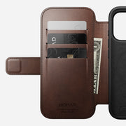 The Nomad Modern Leather Folio for iPhone 17 Pro in Rustic Brown Horween leather features three card slots holding cards and cash, displays NOMAD Horween Leather Co. branding inside, and is MagSafe compatible.