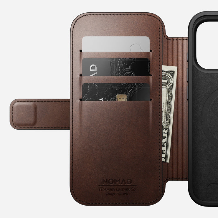 The Nomad Modern Leather Folio for iPhone 17 Pro in Rustic Brown Horween leather features three card slots holding cards and cash, displays NOMAD Horween Leather Co. branding inside, and is MagSafe compatible.