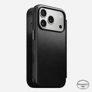 An iPhone 17 Pro is shown in a black Horween leather Nomad Modern Leather Folio case. MagSafe compatible, the case covers the back and sides, exposes three camera lenses, and displays the Horween logo at the bottom right.