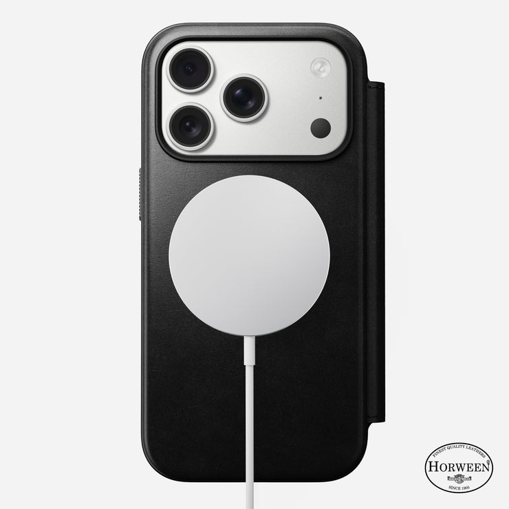 An iPhone 17 Pro with three cameras is in a black Horween leather Nomad Modern Leather Folio; a circular wireless charger attaches to the MagSafe-compatible back, and the Horween logo appears at the bottom right.
