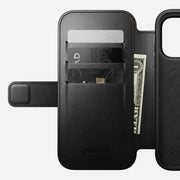 Nomad’s Modern Leather Folio for iPhone 17 Pro in black Horween leather, shown open with three card slots (holding two cards and a folded US dollar bill) and the phone compartment on the right.
